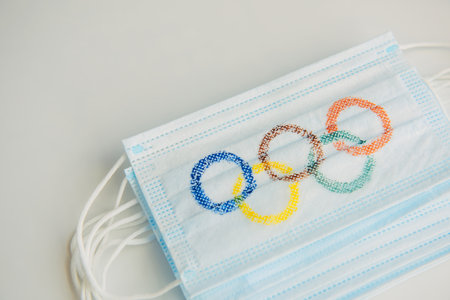 Concept of coronavirus security during 2022 Olympic Games. Olympic rings painted on medical masks lying in a pile on a white background. copyspace. Novosibirsk, Russia - 06.01.2022.のeditorial素材