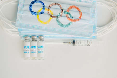Safety of sports competition during covid19 pandemic. Mandatory vaccination of athletes at the Olympics. Mask, vaccine, syringe on white background. Novosibirsk, Russia - 06.01.2022. copyspace.のeditorial素材
