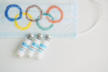 Safety of sports competition during covid19 pandemic. Mandatory vaccination at the Olympics. Medical mask, coronavirus vaccine on white background. copyspace. Novosibirsk, Russia - 06.01.2022.のeditorial素材
