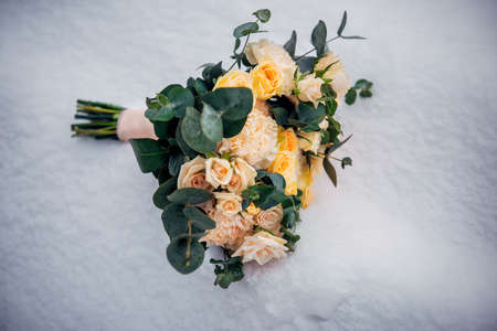 Delicate wedding bouquet of fresh flowers on fluffy snow, close-up. Beige roses on white frozen background. Winter wedding. Copy space.の写真素材