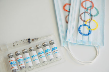 Novosibirsk, Russia - 06.01.2022. Medical masks with Olympic rings, vials with coronavirus vaccine on white background. Concept of virus security at the 2022 Olympics in Beijing.のeditorial素材