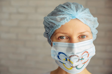 Female doctor in medical mask and cap, close-up, blurred background. Olympic Games during pandemic. Novosibirsk, Russia - 06.01.2022.のeditorial素材