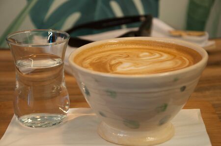 Cup of capuchino in a custom cup with glas of water. Close up.