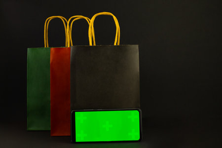 Paper bags and a phone with a green screen on a black background.Black Fridayの写真素材