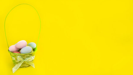 Wide Easter banner. Green basket with colorful eggs on a yellow background.の写真素材