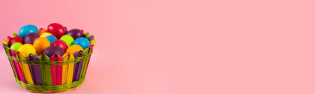 Wide Easter banner. Multi-colored eggs lie in a wicker basket, pink background.