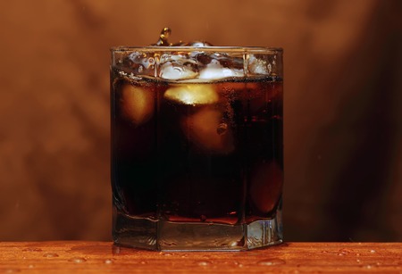 glass of whiskey and ice under the pouring whiskey isolated over brown backgroundの写真素材