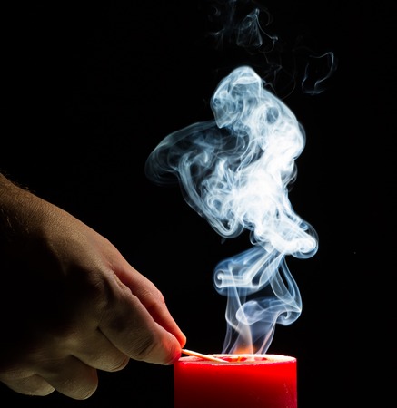 Man's hand is lighting a candle. Smoke on black background