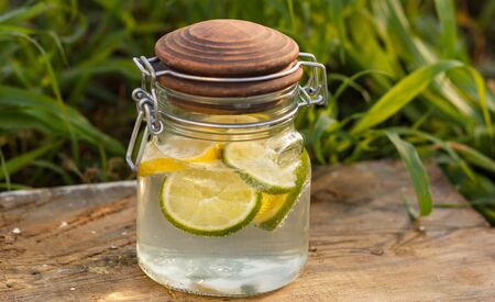 Orange and lemon lemonade in pitchers and glasses on wooden table on natural backgroundの写真素材