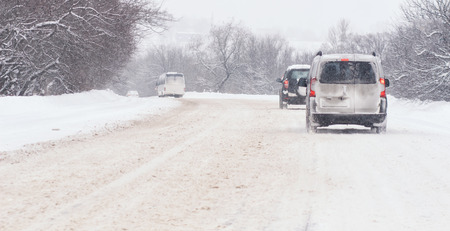 Snow covered road, winter driving with sign - slipperyの写真素材