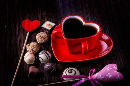 top view image of colorful heart shape chocolates, fabric heart, vintage photo camera and cup of coffee on wooden table. valentine's day celebration concept. retro filteredの写真素材