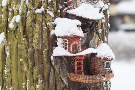 Red barn birdhouse covered in snow with snow covered trees blurred in backgroundの写真素材