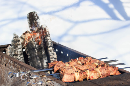 Outdoors winter barbecue party with a person wearing knitted woollen gloves cooking sausages over hot coals in a BBQ, close up viewの写真素材