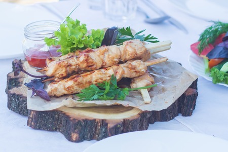 Chicken skewers with slices of apples and chili sauce on a wooden slice