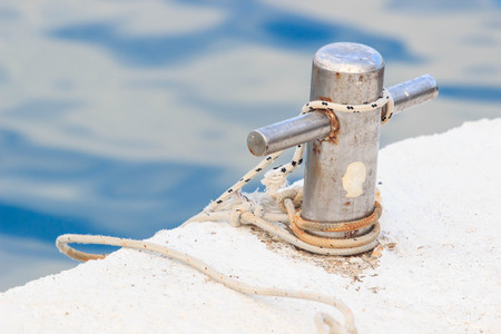 Close-up of a mooring rope with a knotted end tied around a cleat on a wooden pier.の写真素材