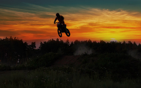 Blurred silhouette of motor cross rider jumping on the mountain in sunrise.の写真素材