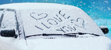 Heart drawn on a car windshield covered with fresh Christmas snowの写真素材