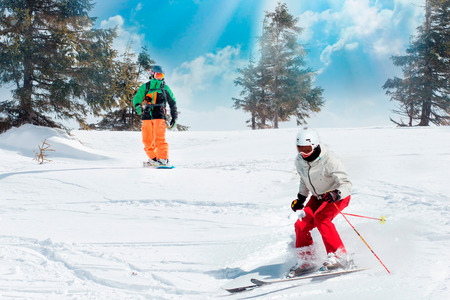 Skiers and snowboarders riding on a ski resort on snowy winter mountain with fir-tree background scenic view.の写真素材