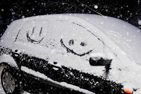 simple picture of a smile carved in the snow upon a window of a black car,の写真素材