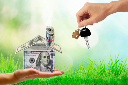 Money bags on hand and house key in hand and Sunlight represent Exchange or sell or contract for renting a house or real estate. Saving money or investing to buy a home or loan.の写真素材