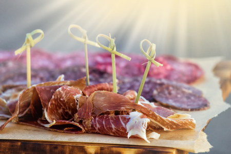 thin slices of prosciutto with olives and salami on wooden cutting boardの写真素材