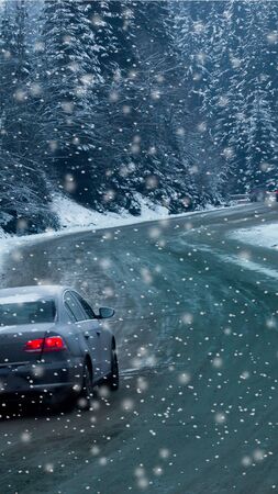 Car and falling snow in winter on forest road with much snow. vertical