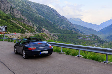Hospental, Switzerland - July 5, 2025: Blue Porsche 911 convertible on mountain pass Gotthard Pass and panorama view towards valley Urseren in the Swiss canton of Uriのeditorial素材