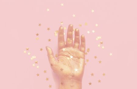 Gold painted palm with star confetti on a pastel pink background. Christmas festive backgroundの写真素材
