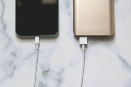 flat lay of smartphone charging from a portable power bank on a marble table background