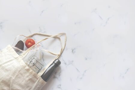 zero waste concept reusable shopping bag with metal bottle, glass jar and mesh bag with avocado and tomato on marble background with copy spaceの写真素材