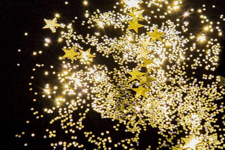 gold shiny glitter and star confetti on black background for Christmas backdrop