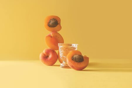 balancing apricots still life on a yellow background front view with ctystal shot glass of vodkaの写真素材