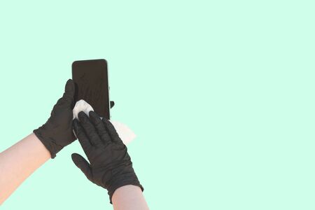 hands wearing protective latex black gloves wiping smartphone with antibacterial wipes covid prevention conceptの写真素材