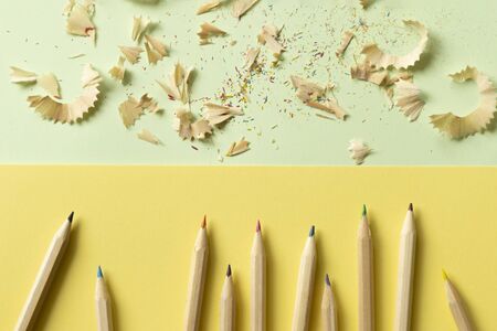 color pencil shavings and pencils on a color block mint green and yellow background