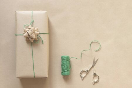 zero waste christmas concept present wrapped in plain recycled paper with green thread and scissors on beige background with copy spaceの写真素材