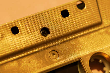 macro detail of gold cassette tape on a beige background with shadow selective focus retro backdrop for your projectの写真素材