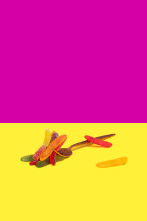 metalic fork with jelly worms on a vertical yellow and purple color block background for halloween