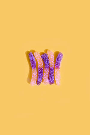 Yellow and purple sugar coated jelly worms on a yellow background with shadowの写真素材