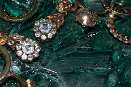 gold rings and earrings with crystal on a transparent gel texture on emerald green background with copy space with selective focusの写真素材