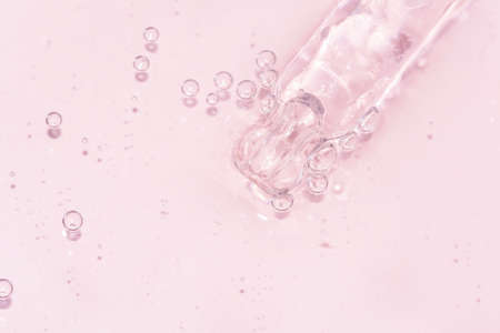 detail of a pipette with pouring serum and droplet with shadow on a pink backgroundの写真素材