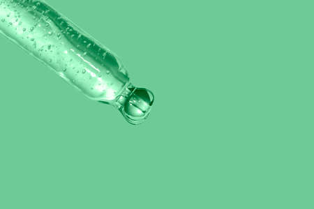 macro of pipette with pouring liquid on mint background luxury skin care treatment concept toned trendy color green ashの写真素材