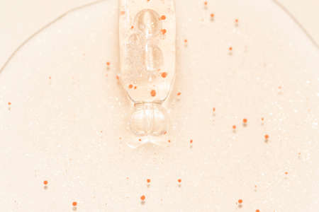 close up macro of pipette dropper with liquid with particles on a beige background luxury serum...
