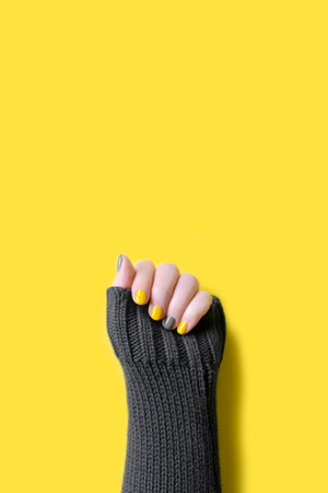Detail of womans hand wearing gray sweater with trendy colors illuminating yellow and ultimate grey manicure nailsの写真素材