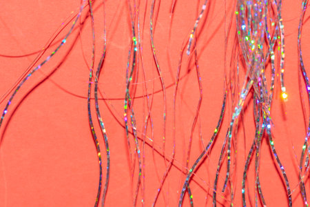 festive holographic tinsel fringe detail on coral red background with selective focus