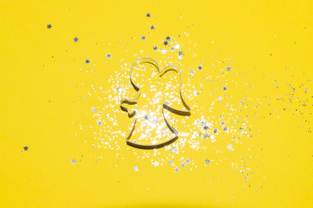 silver Christmas themed cookie cutter on a bright yellow background with silver glitter and star confettiの写真素材