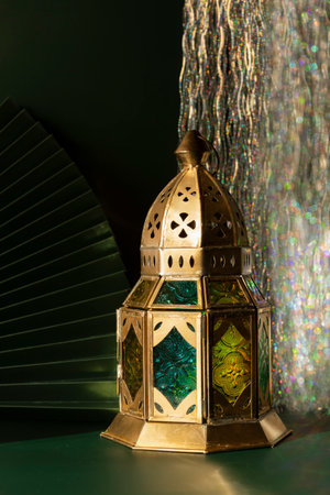 Beautiful traditional Moroccan lantern on a dark emerald background with paper fan and tinsel bokeh lightsの写真素材