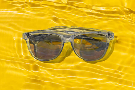 gray sun glasses under yellow water with sun glare and waves