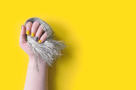 Detail of womans hand holding silver tinsel fringe with trendy colors illuminating yellow and...