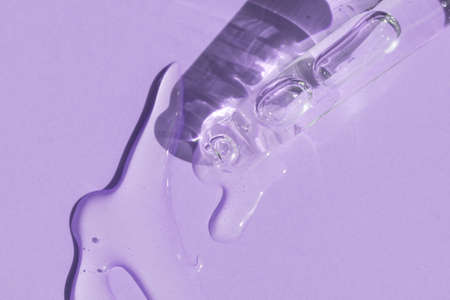 close up of pipette with pouring liquid serum and shadows on purple backgroundの写真素材