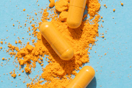 orange curcumin turmeric pills with powder and shadow on blue backgroundの写真素材